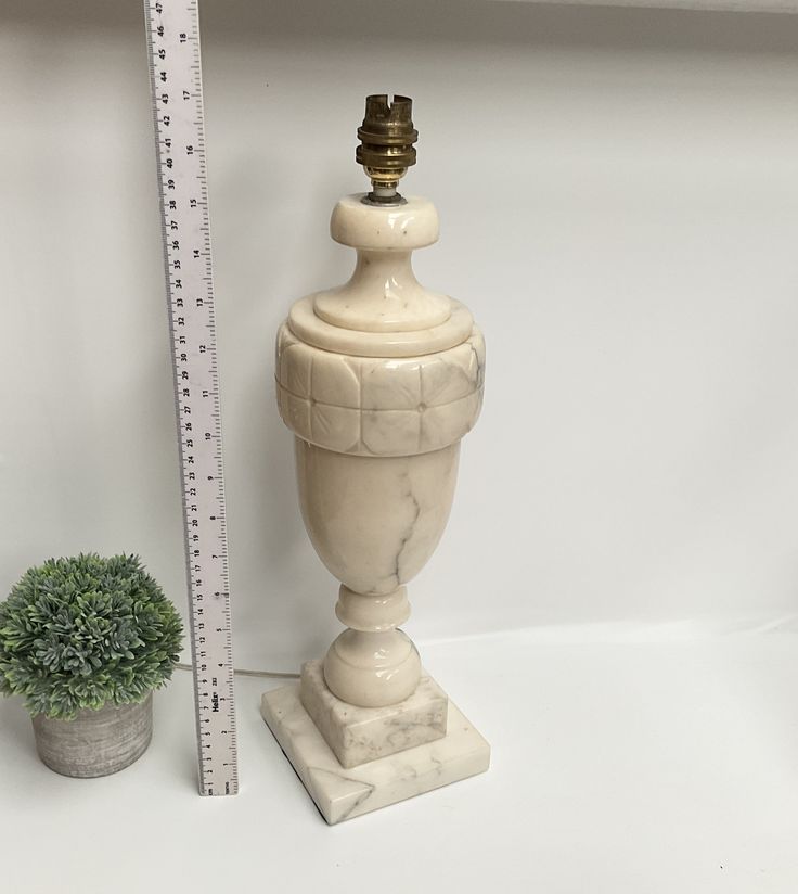 a tall white vase sitting next to a potted plant on top of a table