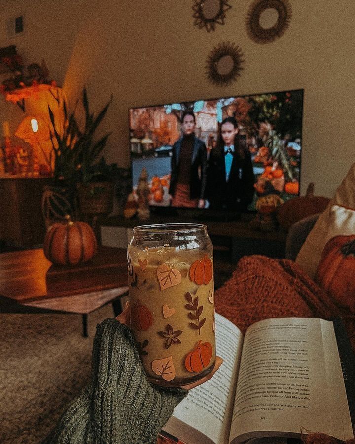 a person holding an open book in front of a television with pumpkins on it