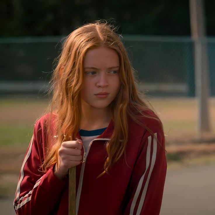 a girl with long red hair is holding onto her jacket and looking at the camera