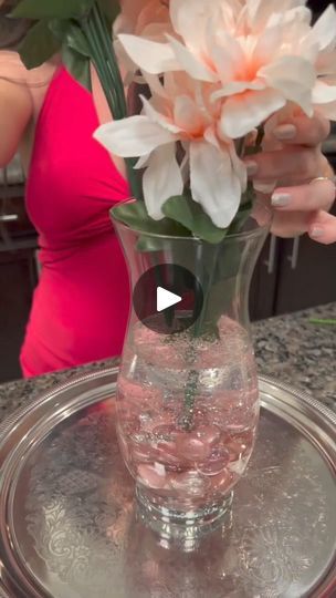 a vase with water and flowers in it on a tray next to a woman's hand