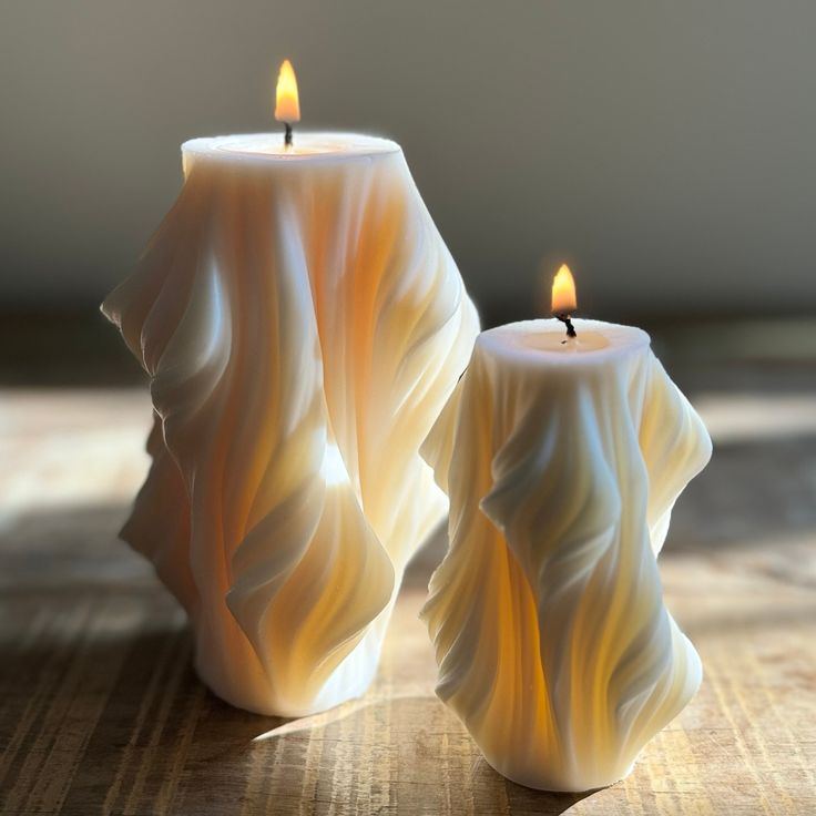 two white candles sitting on top of a wooden table