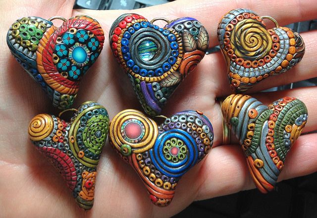 four colorful heart shaped beads are held in someone's hand, with the background black