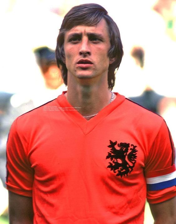 a man in an orange shirt standing on a soccer field with his head turned to the side