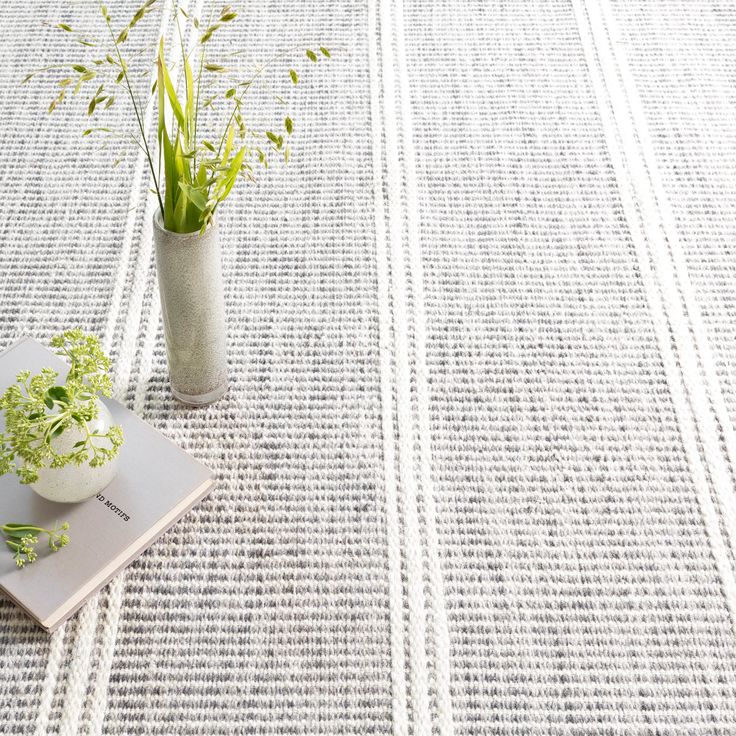 a white book and some plants on a table with a striped rug in the background