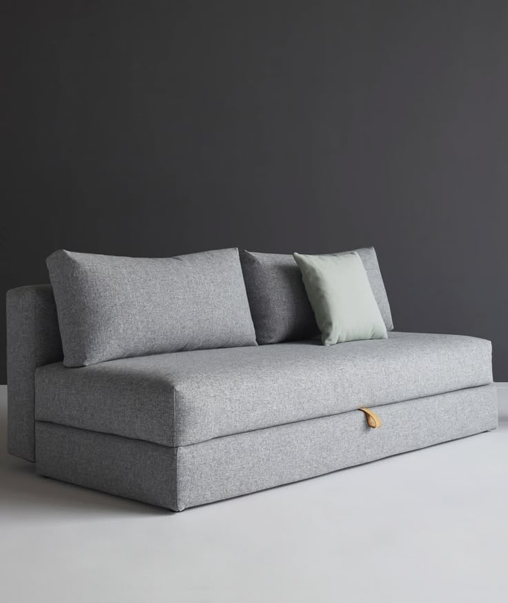 a grey couch with two pillows on it and a gray wall in the back ground