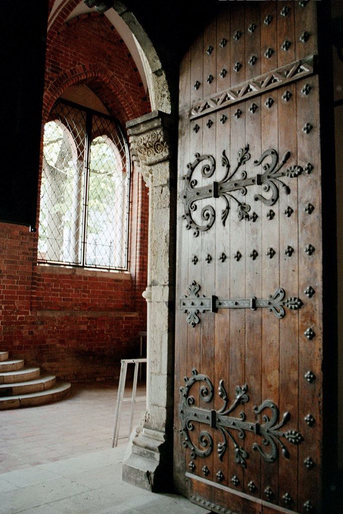 an old wooden door with iron work on it in front of a brick wall and stairs