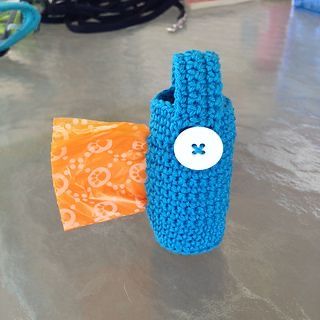 a blue crocheted bottle with a white button on the side and an orange bag next to it