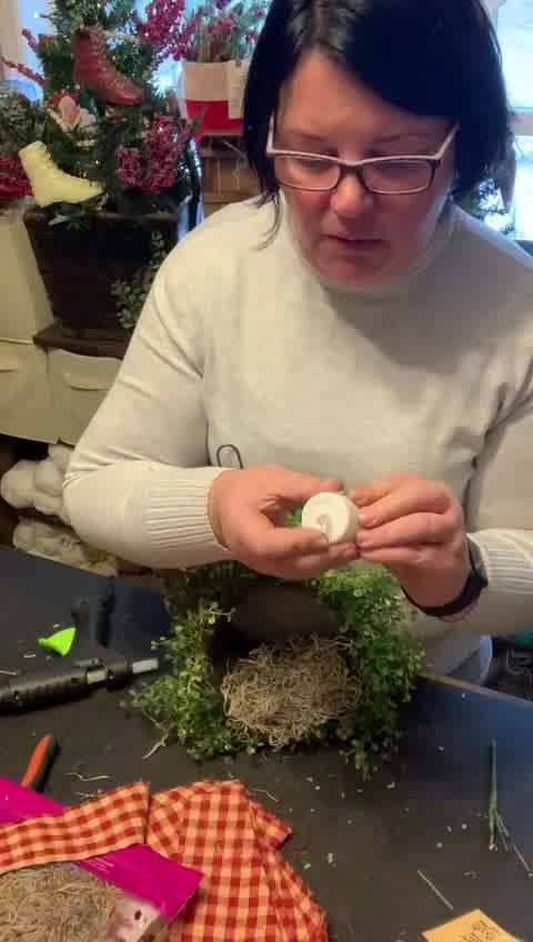 a woman is making a wreath out of twigs and other items on a table in front of her