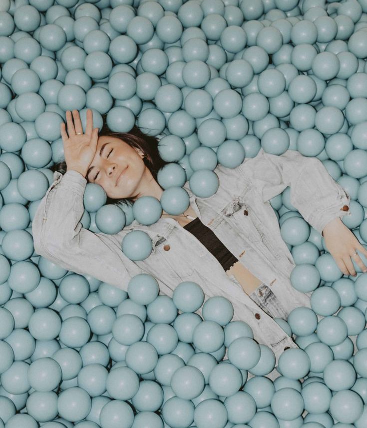 a man laying in a ball pit with his hands on his head and eyes closed