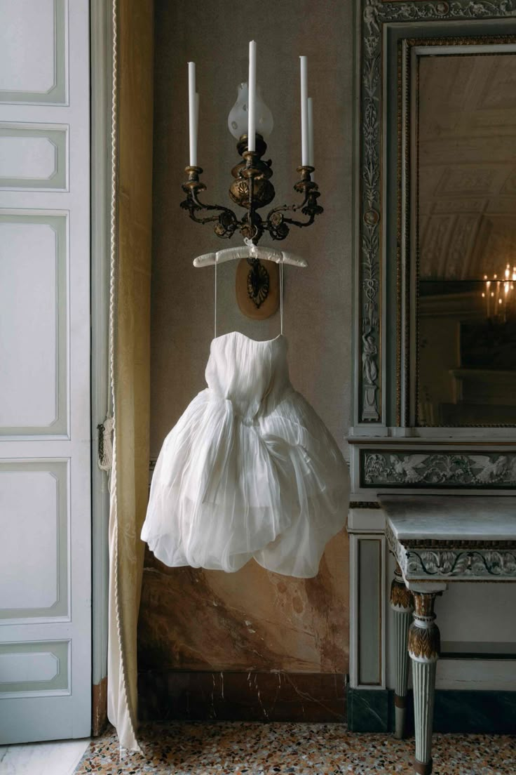 a white dress hanging from a wall with candles