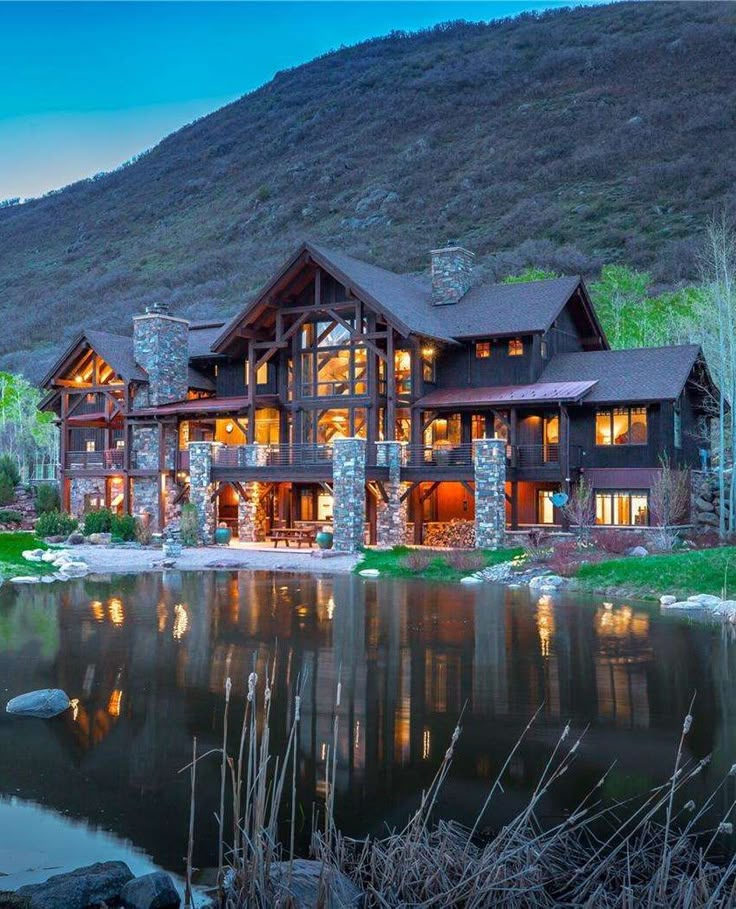 a large house sitting on top of a lush green hillside next to a lake at night