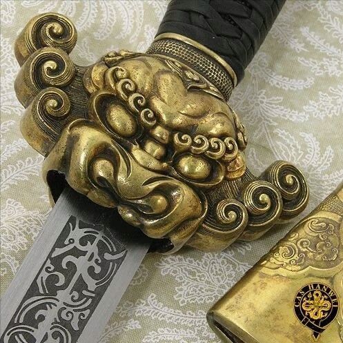 a gold colored dragon head knife next to a black and white patterned tablecloth with an ornate design on it