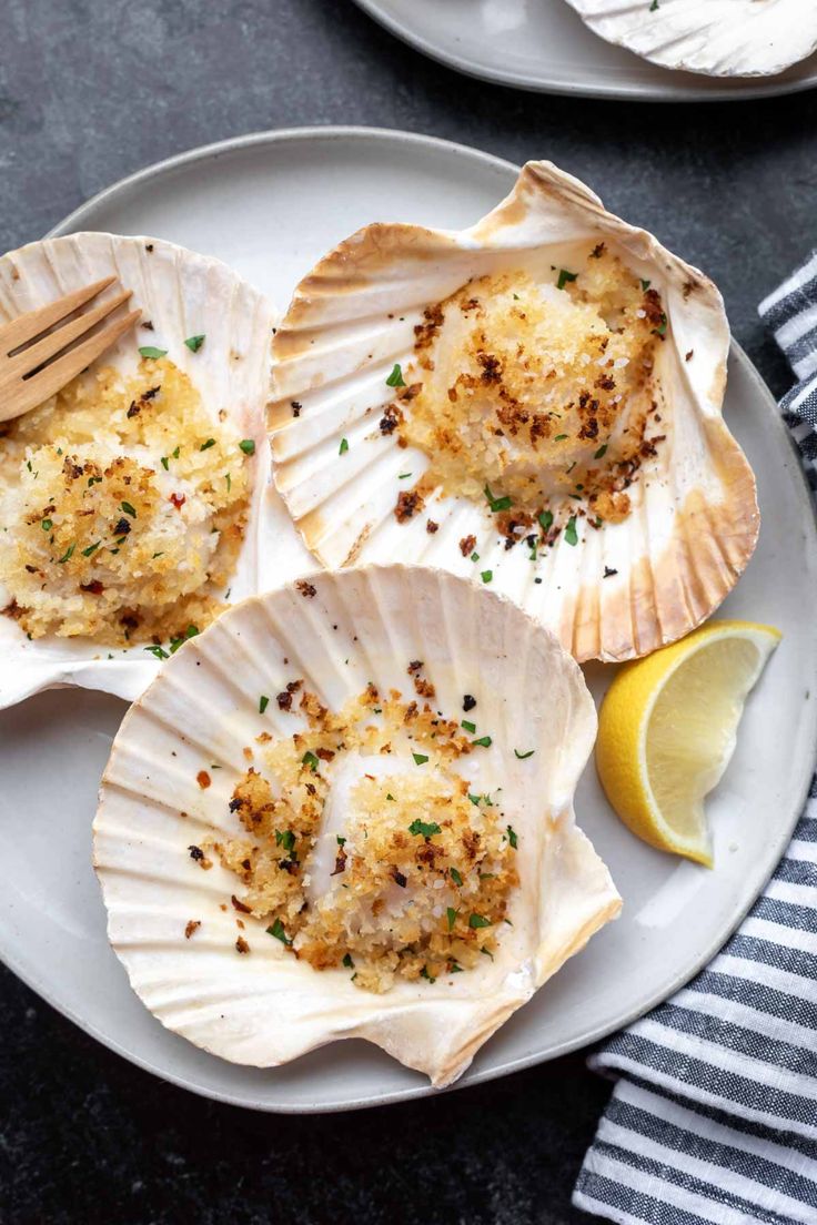 three scallops on a plate with lemon wedges and parmesan cheese