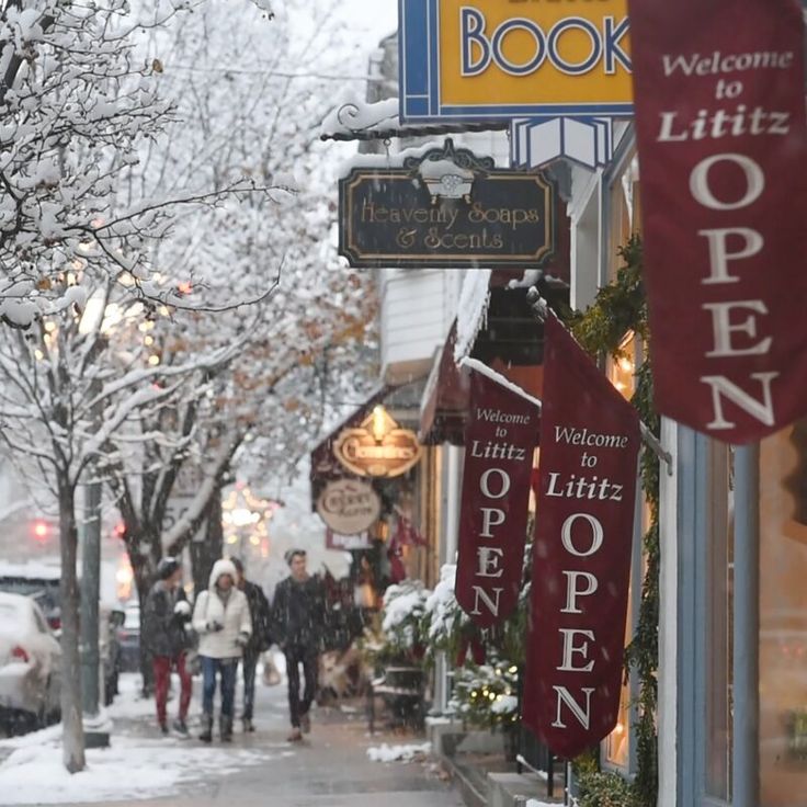 people are walking down the sidewalk in front of bookshops on a snowy day