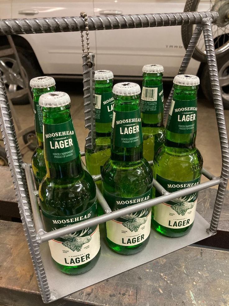 six bottles of lager sitting on a metal rack in front of a white car