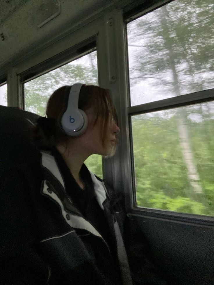 a woman with headphones sitting in a train car looking out the window at trees