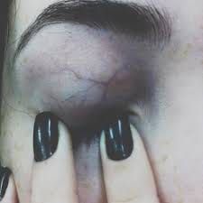 a person with black fingernails and fake nails holding their hands up to the camera's eye