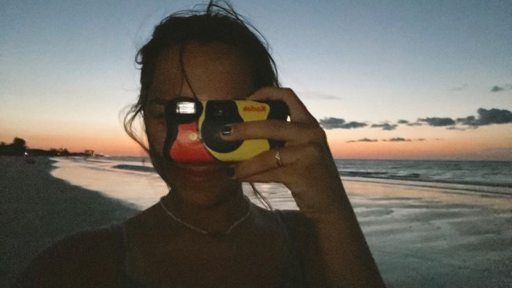 a woman taking a photo with her cell phone at the beach during sunset or sunrise