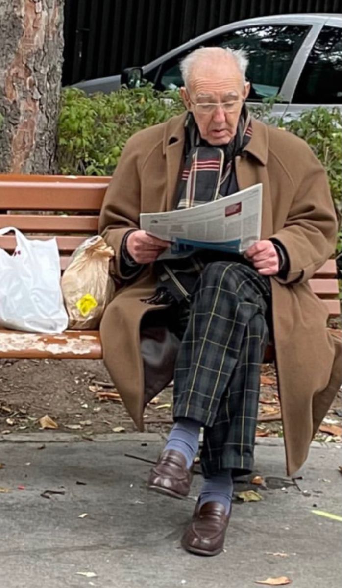 an old man sitting on a bench reading a newspaper