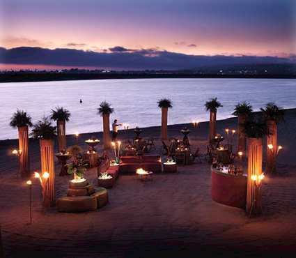 an outdoor dining area next to the water at dusk with lit candles and palm trees