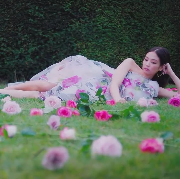 a woman laying in the grass with pink flowers on her stomach and dress blowing in the wind