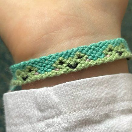 a close up of a person's wrist wearing a green and black crochet bracelet