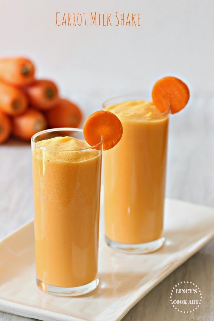 two glasses filled with carrot juice on top of a white plate next to oranges