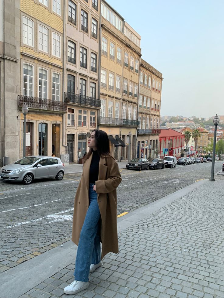 a woman is standing on the sidewalk in front of some buildings and looking at something