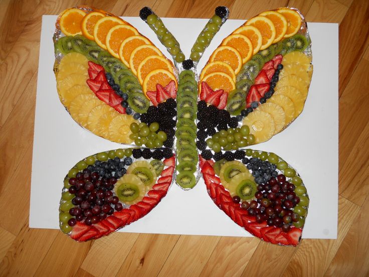 a butterfly made out of fruit on top of a white paper sheet with wood flooring