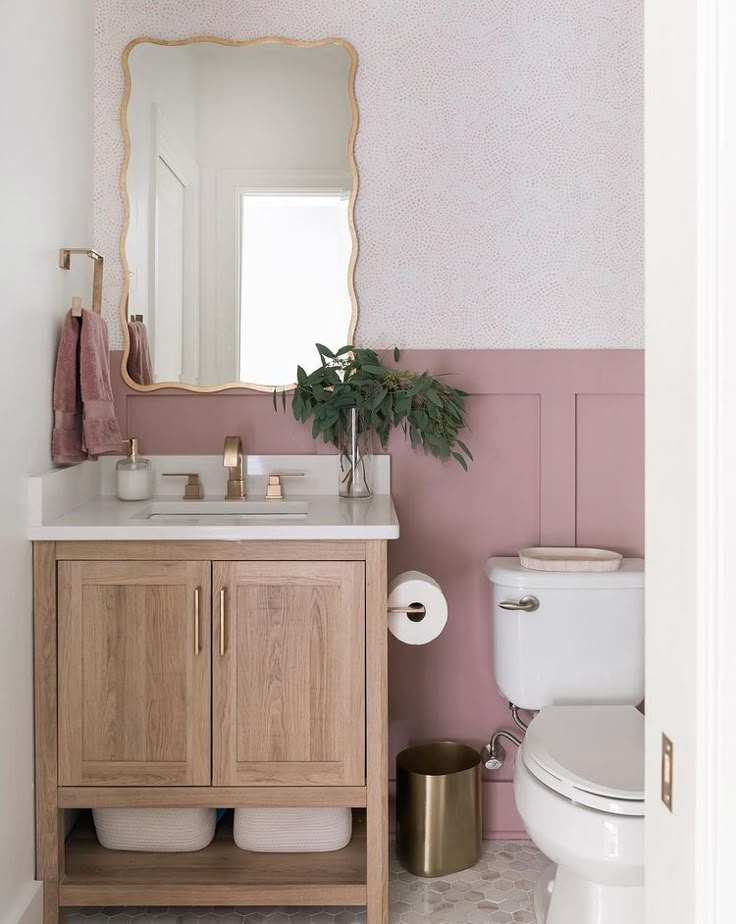 a white toilet sitting next to a wooden sink vanity in a pink and white bathroom