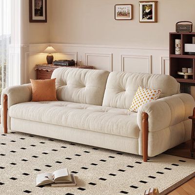 a living room with a white couch and book shelf on the floor next to a window