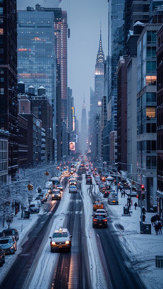 a city street filled with lots of traffic next to tall buildings and snow covered ground