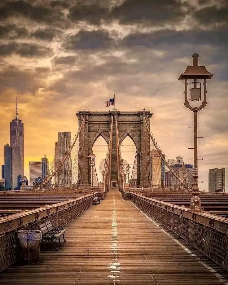 an empty bench sitting on the end of a bridge with a city skyline in the background