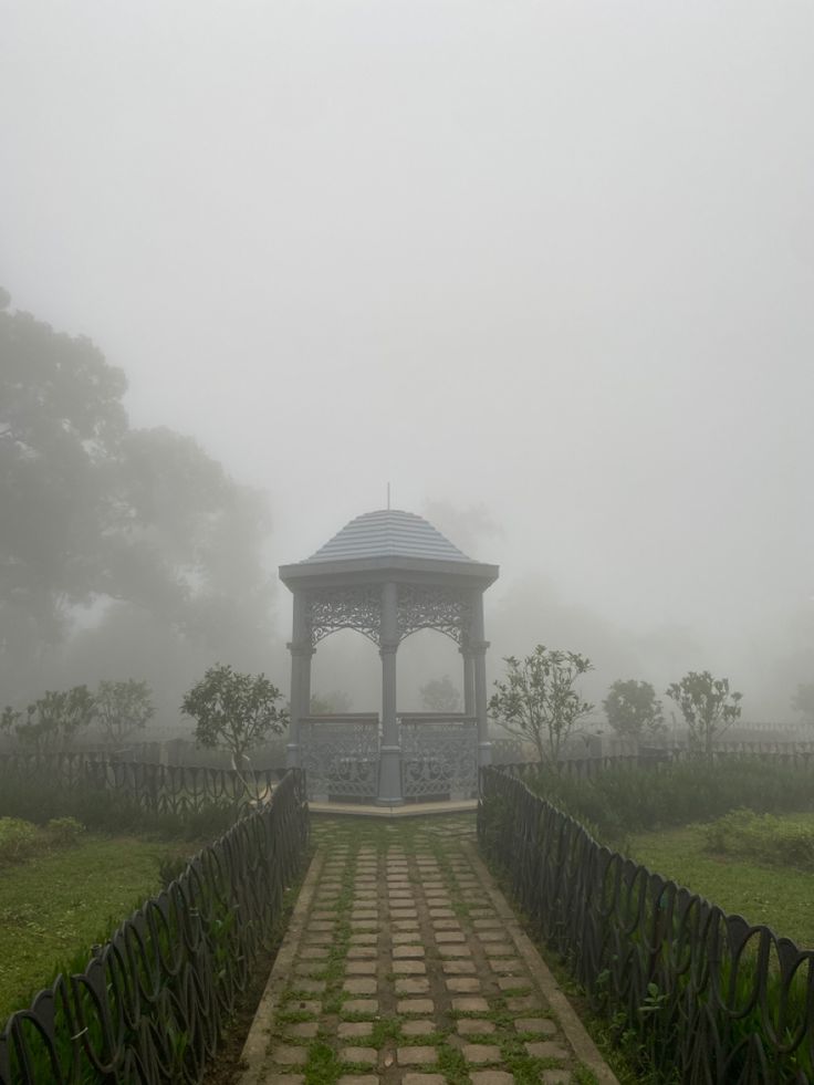 a gazebo in the middle of a foggy field with stone walkways leading to it