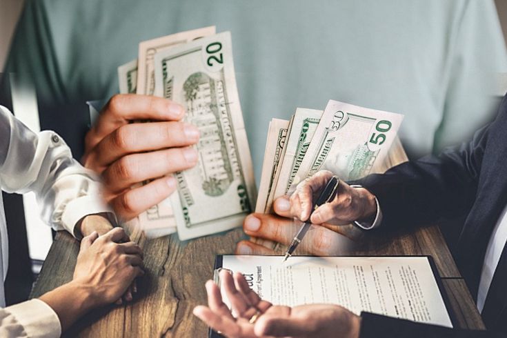 three people sitting at a table with stacks of money in front of them, and one person holding a pen