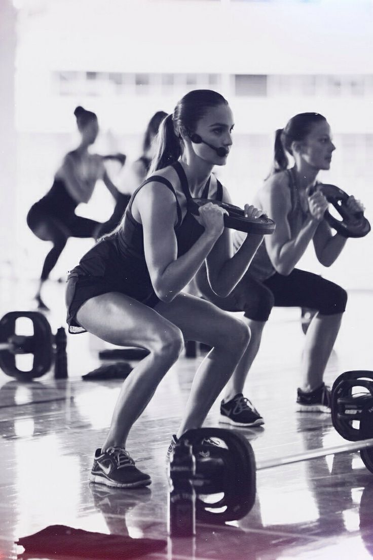 two women are squatting while holding kettlebells in a crossfit gym