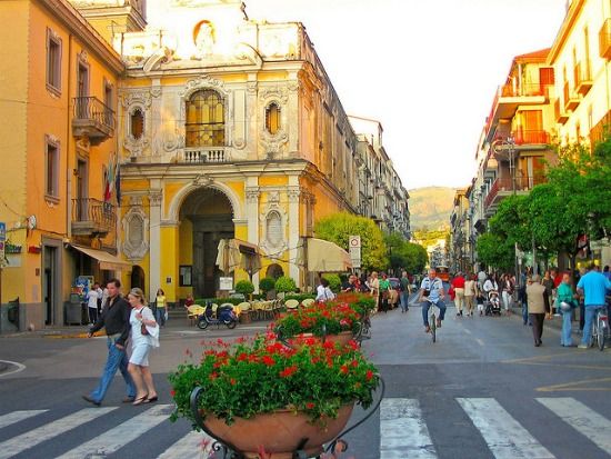 people are walking down the street in front of buildings with flowers growing out of them