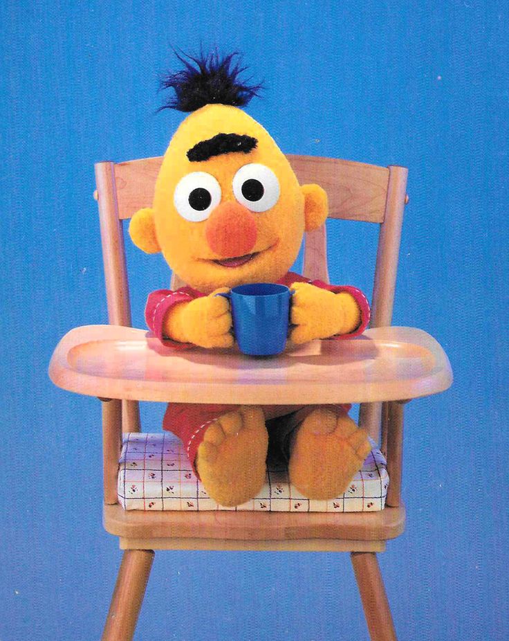 a sesame character sitting in a wooden chair with a cup