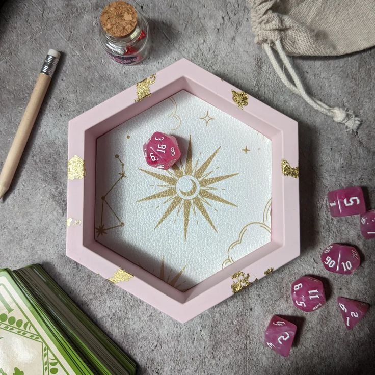 a pink and gold dice board with numbers on it next to other dice pieces, including one in the shape of a hexagon