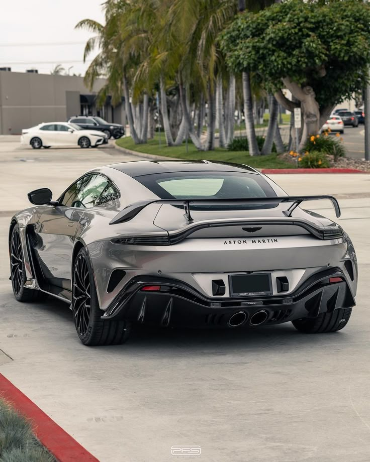 a silver sports car parked in a parking lot with palm trees and buildings behind it