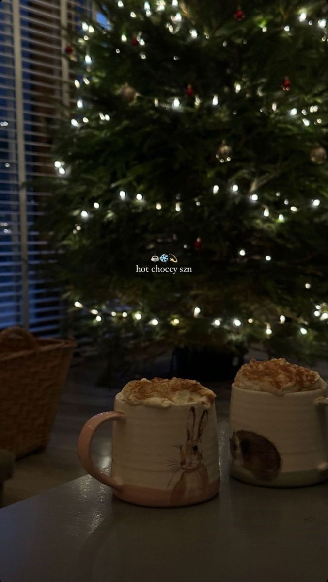 two mugs sitting next to each other on a table in front of a christmas tree