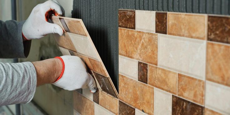 a man is working on a tile wall with his hands and gloves are holding the tiles