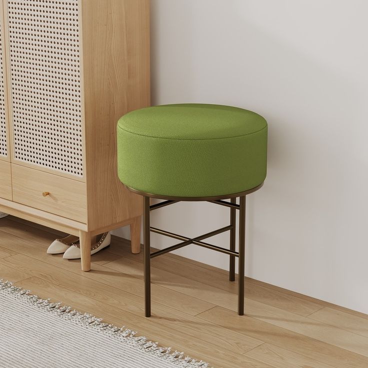 a green stool sitting in front of a white wall next to a cabinet and rug