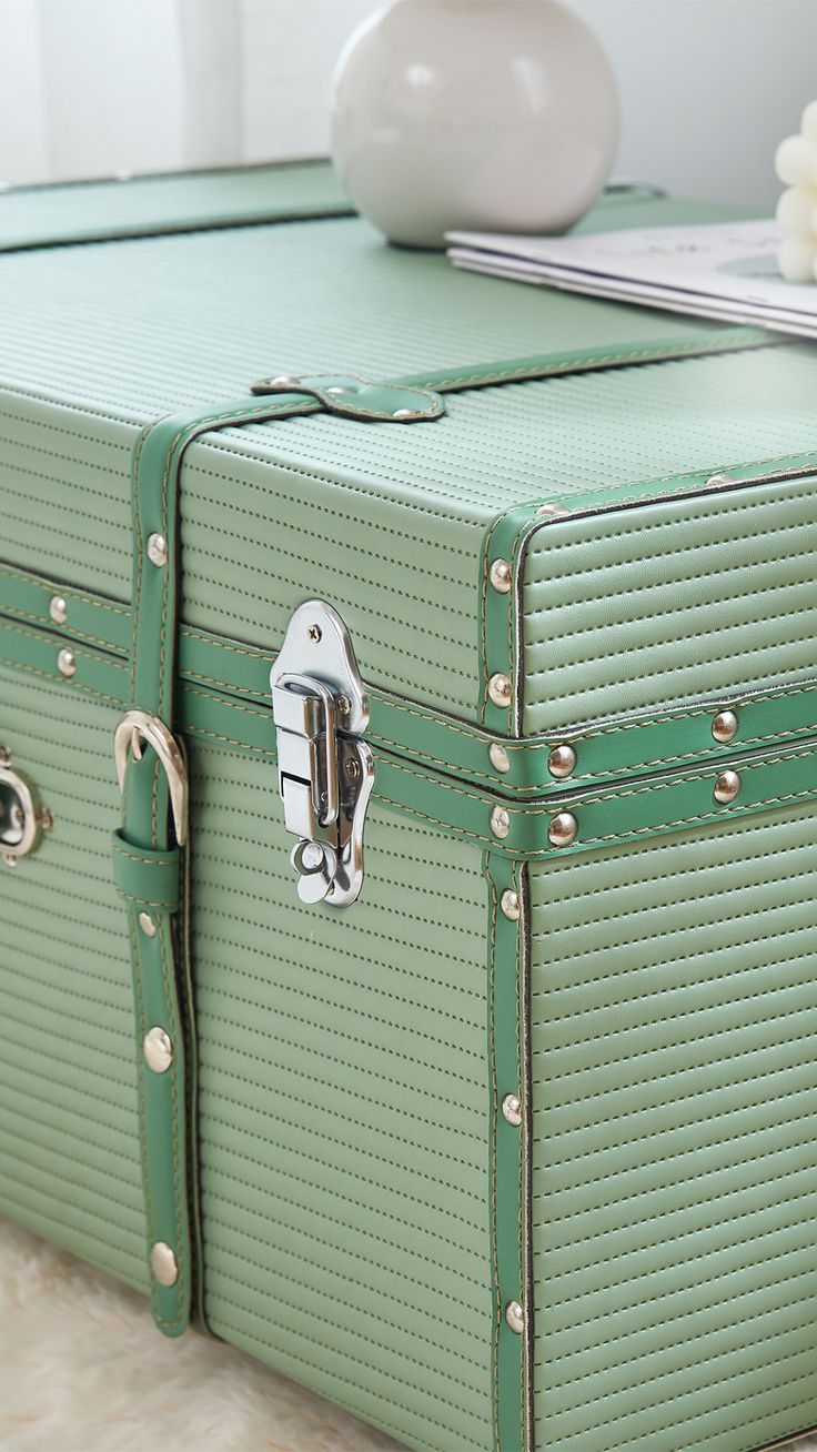 a green suitcase sitting on the floor next to a white vase and other items in front of it