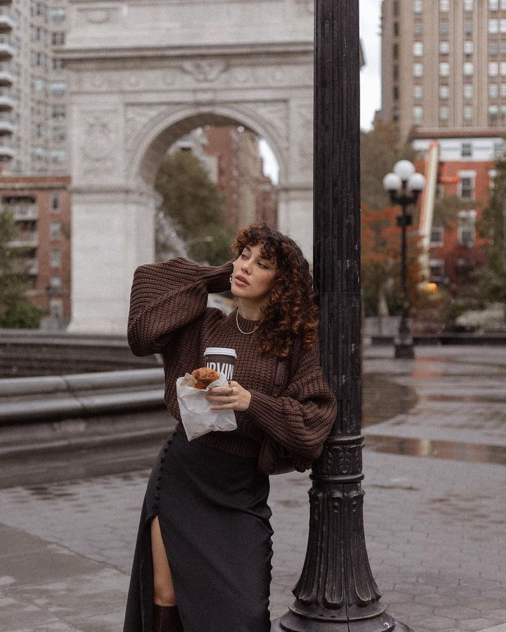 a woman leaning against a lamp post while eating