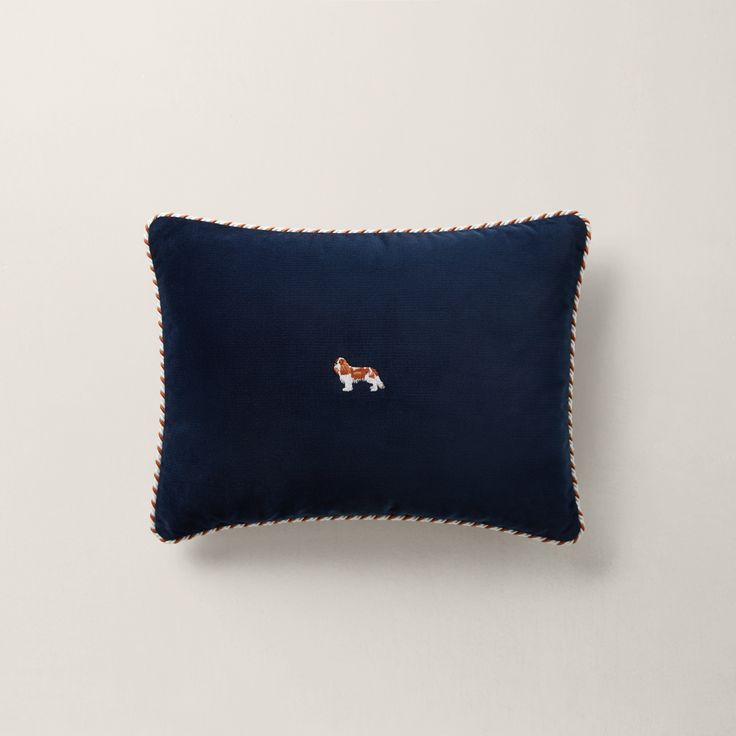 a blue pillow with a dog embroidered on the front and side, sitting against a white wall