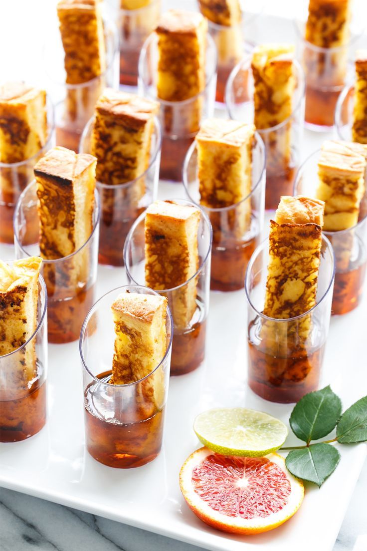 small glasses filled with different kinds of desserts on a white tray next to sliced grapefruit