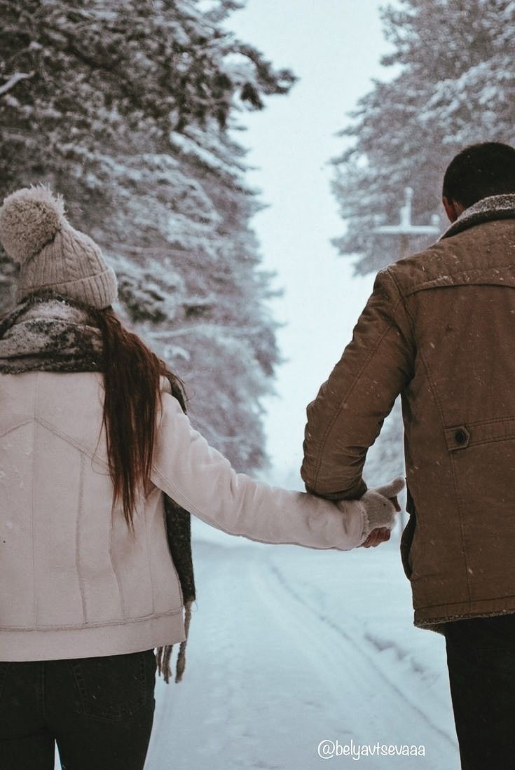 a man and woman holding hands walking down a snow covered road in the wintertime