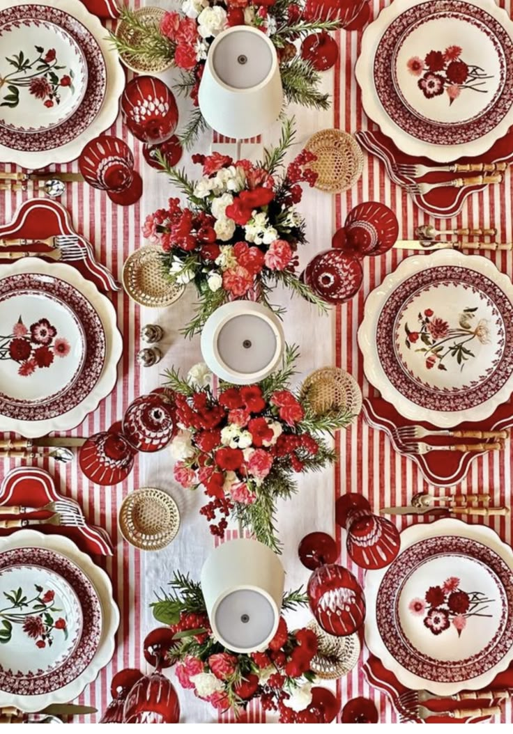 the table is set with red and white plates, cups, and flowers on it