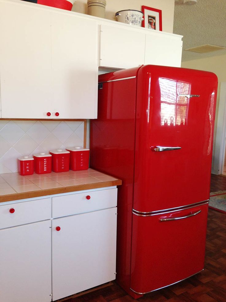 a red refrigerator freezer sitting in a kitchen next to white cabinets and cupboards